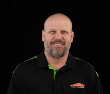 Man wearing a black SERVPRO shirt with no hair and smiling.
