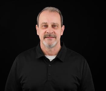 Man wearing a black SERVPRO shirt with gray hair and smiling.
